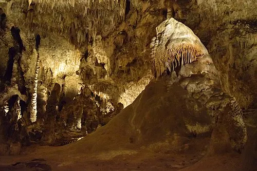 Visitors on the lit Big Room trail near a caveman rock feature, the underground setting where the cave snack rest area sits 750 feet down.
