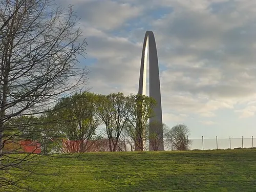 Sunrise over the landscaped Gateway Arch grounds, with paved pathways and trees beneath the Arch.
