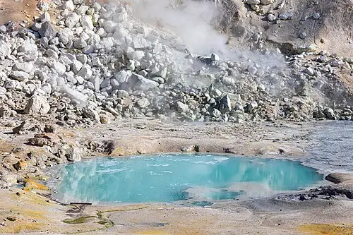 An aquamarine boiling pool in the Bumpass Hell hydrothermal basin, steam rising over pale mineral ground.