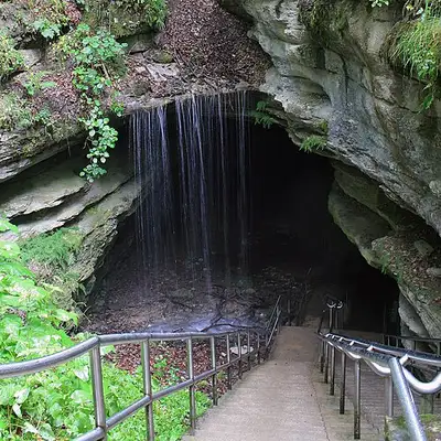 The natural Historic Entrance to Mammoth Cave, a rock opening in the forested Green River valley hillside.