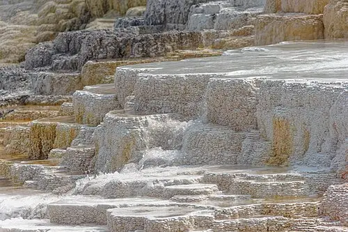 Stepped travertine terraces of Mammoth Hot Springs with water flowing over orange and white mineral deposits.
