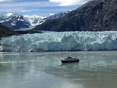 The Bartlett Cove day boat holds position below the tall ice face of Margerie Glacier, the boat small against the glacier for scale.