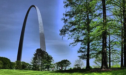 People walking the green Gateway Arch grounds beneath the Arch, near the North Gateway and the Explorers Garden.