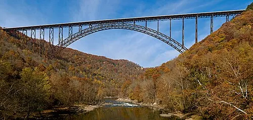 The New River Gorge Bridge, a long single-span steel arch carrying U.S. Route 19 high above the forested gorge.