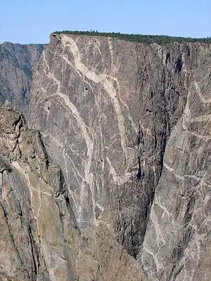 Painted Wall in Black Canyon of the Gunnison, a sheer dark cliff streaked with pink pegmatite veins dropping to the river far below.