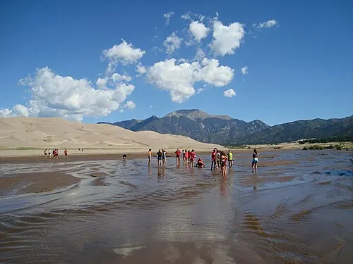 Wide view of the Great Sand Dunes dunefield with Medano Creek in front and the Sangre de Cristo Mountains behind.