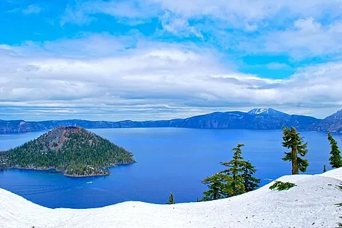 Wizard Island, a forested volcanic cinder cone, standing in the blue water of Crater Lake seen from the rim.