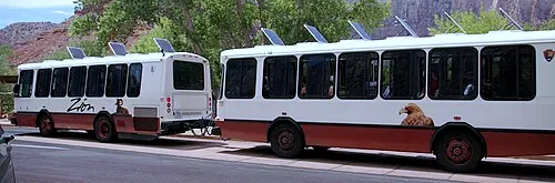 A Zion National Park shuttle bus on the canyon road below the red sandstone cliffs, the system that connects Springdale to the canyon.