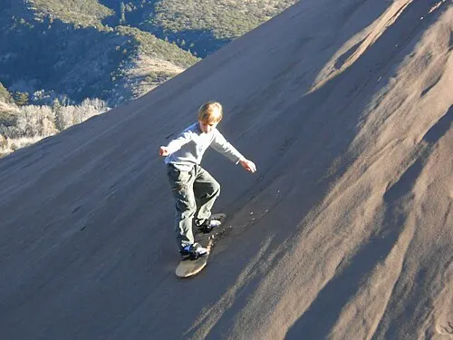 A child sandboarding down a steep dune face at Great Sand Dunes.