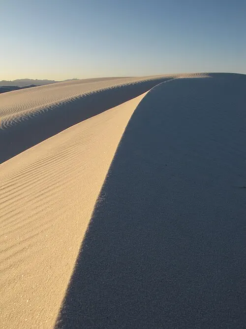 A steep sunlit gypsum dune face of the kind families sled at White Sands.