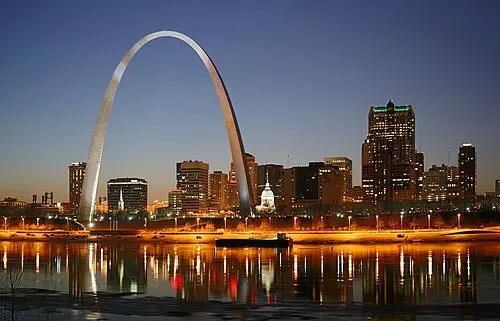 The downtown St. Louis skyline at night with the lit Gateway Arch beside the Mississippi River.