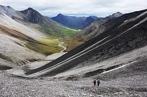 A backpacker walking off-trail across open tundra in Gates of the Arctic, the kind of country where parties camp on river gravel bars.
