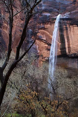 A thin seep waterfall falling off a sandstone overhang at the Lower Emerald Pool, where the trail passes behind the water.