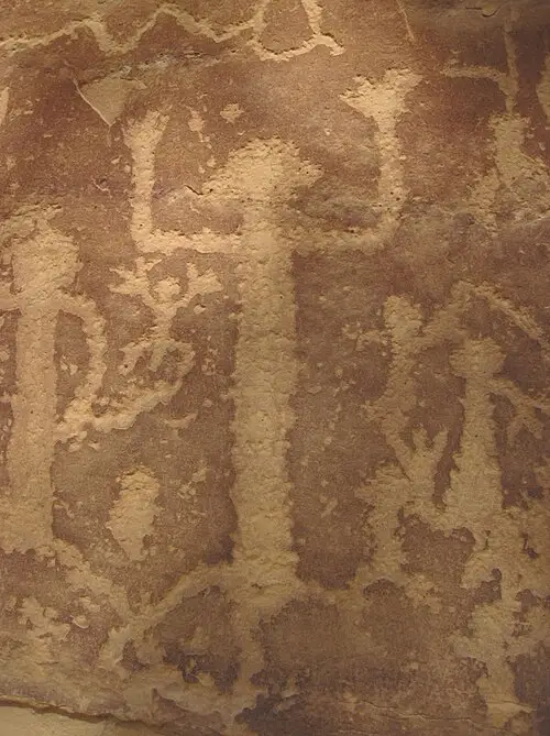 Ancestral Puebloan petroglyphs pecked into the sandstone at the end of the Petroglyph Point Trail, including a spiral and human figures.