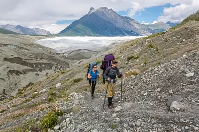 Hikers on the mostly level Root Glacier Trail leading from Kennicott toward the white ice, the most family-realistic hike in the park.