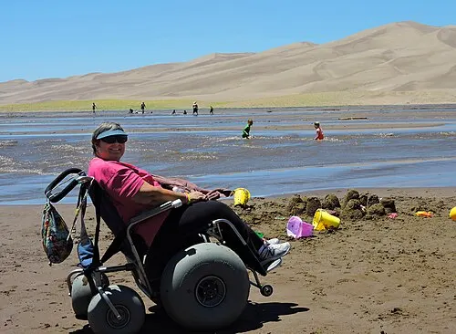 A visitor using a sand wheelchair beside Medano Creek at the main dunes day-use area.