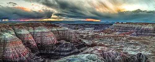 Low sunlight over banded badlands at sunset from a Painted Desert rim overlook, Petrified Forest National Park.