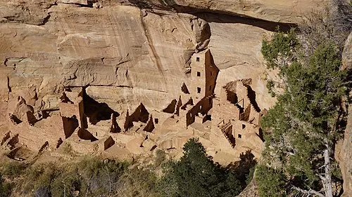 An Ancestral Puebloan cliff dwelling seen across a canyon in a sandstone alcove, the kind of across-canyon view reached from Soda Canyon Overlook.