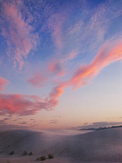 Soft pastel clouds over the white dunes at golden hour, the window for a ranger-led sunset walk.