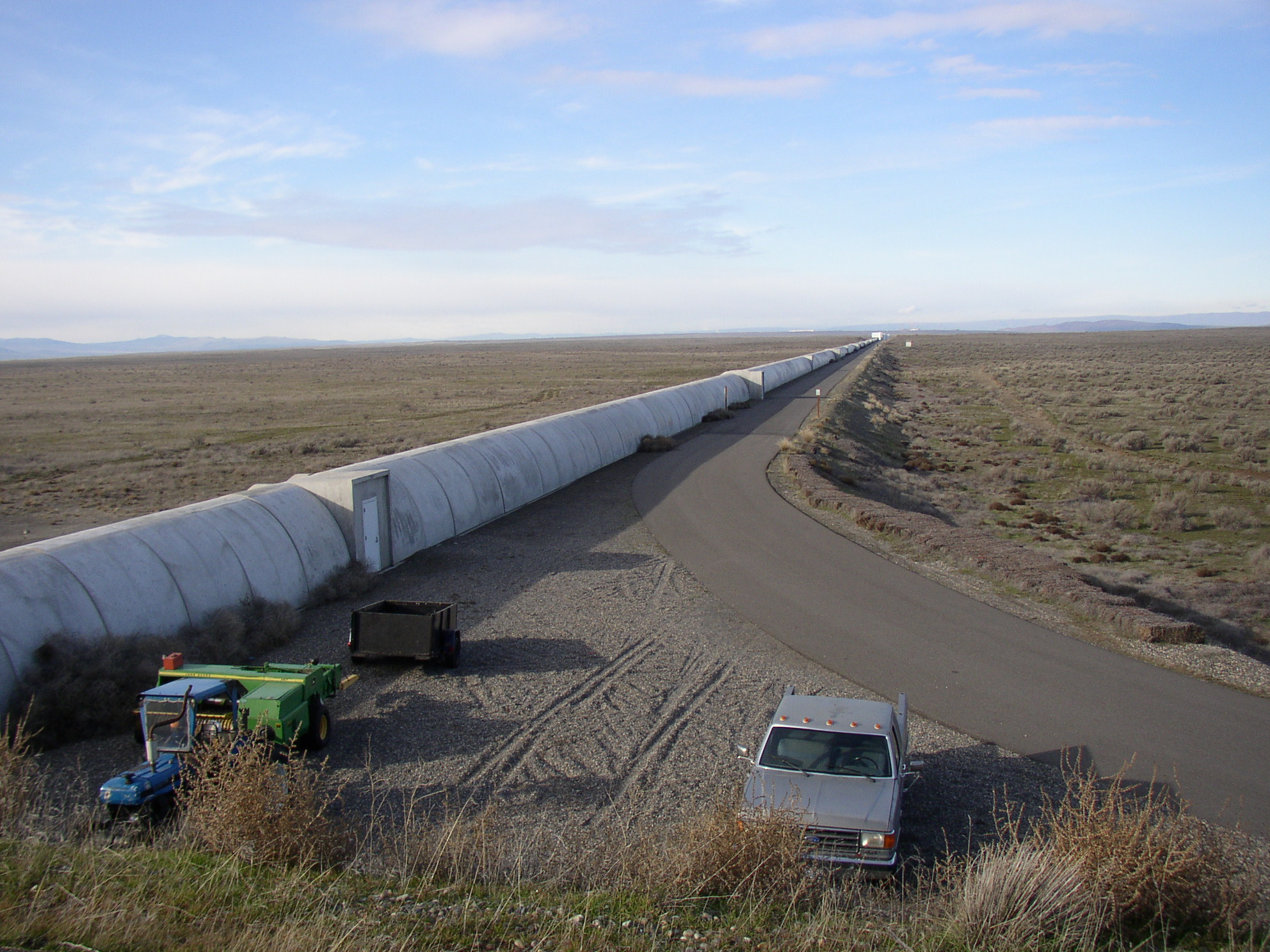 Aerial view down the four-kilometer northern arm of the LIGO Hanford interferometer, with the eastern arm meeting it at the corner station and the shrub-steppe of the Hanford Reach stretching out behind.